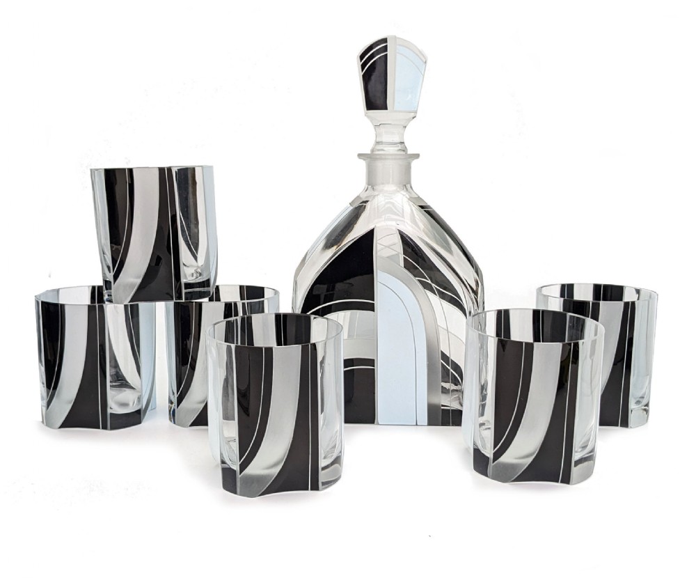 An Art Deco clear glass decanter set with six matching glasses, decorated with black, silver, and pale blue enamelled geometric shapes.