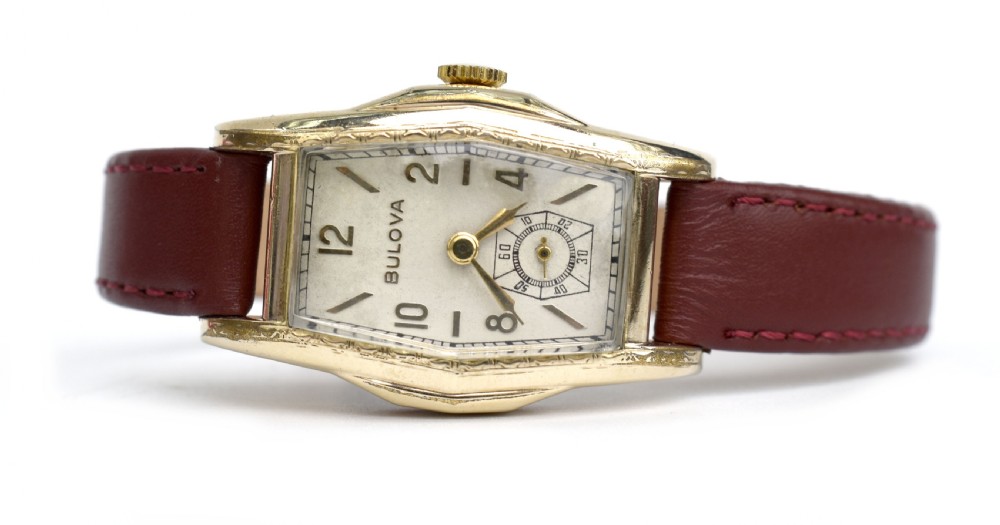 An Art Deco Bulova gents wristwatch featuring a gold-tone tonneau case with engraved side detailing, a cream dial with gold numerals, and a burgundy leather strap. View III