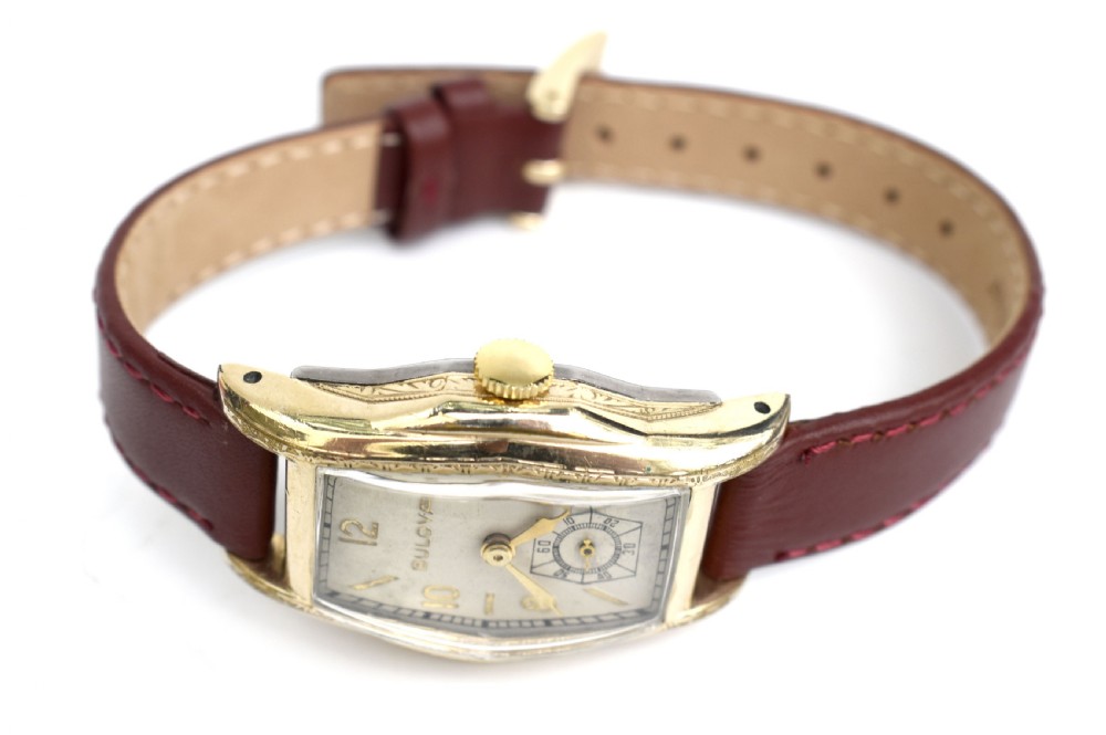 An Art Deco Bulova gents wristwatch featuring a gold-tone tonneau case with engraved side detailing, a cream dial with gold numerals, and a burgundy leather strap. View IV