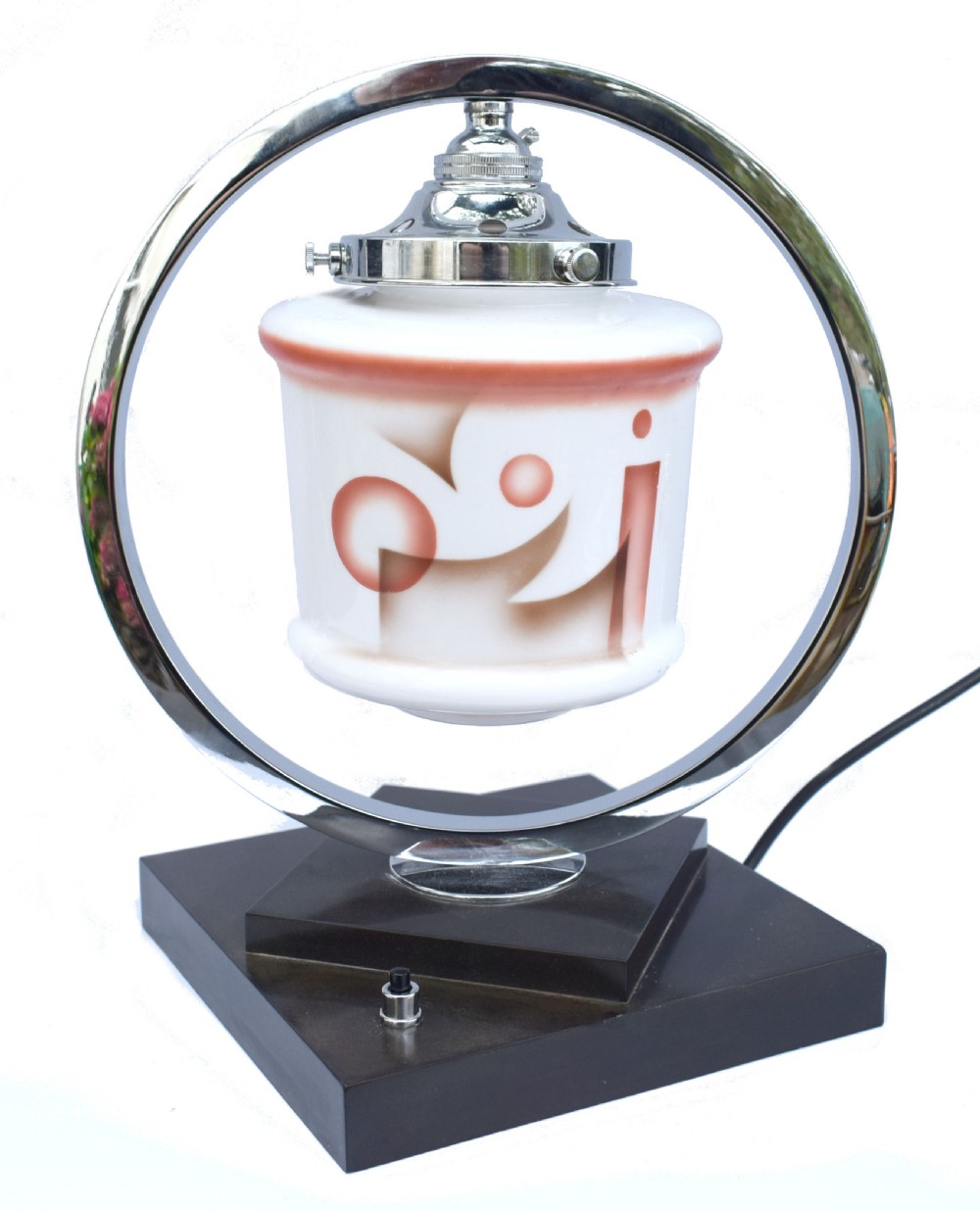 An Art Deco table lamp featuring a circular chrome hoop frame around a patterned glass shade, set on a dark brown stepped Bakelite base.