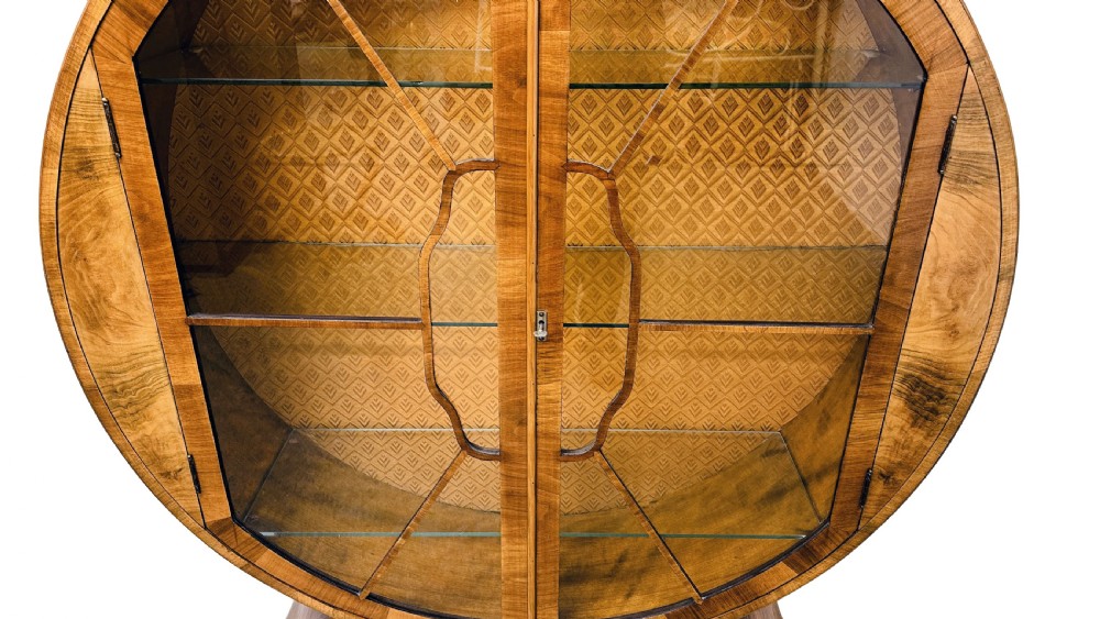 An Art Deco circular walnut display cabinet featuring two glazed doors with geometric astragal glazing bars and interior glass shelves. View IV