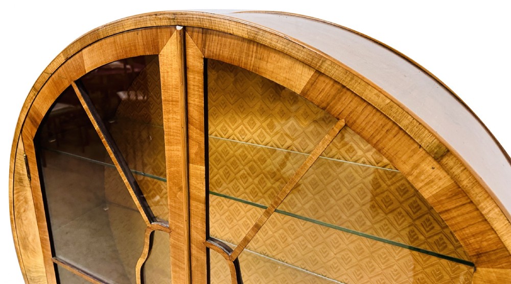 An Art Deco circular walnut display cabinet featuring two glazed doors with geometric astragal glazing bars and interior glass shelves. View X