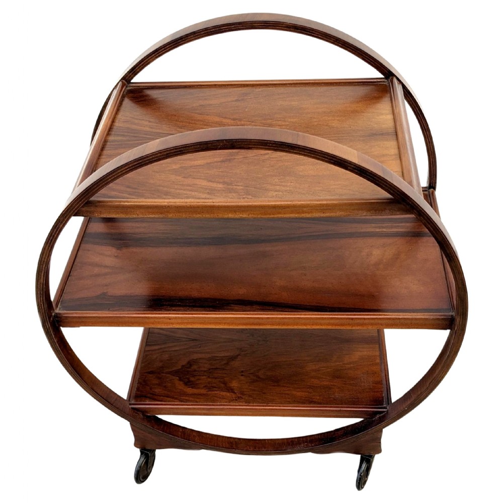 An Art Deco circular walnut drinks trolley featuring three rectangular tiers enclosed within a sweeping circular frame on small castors.