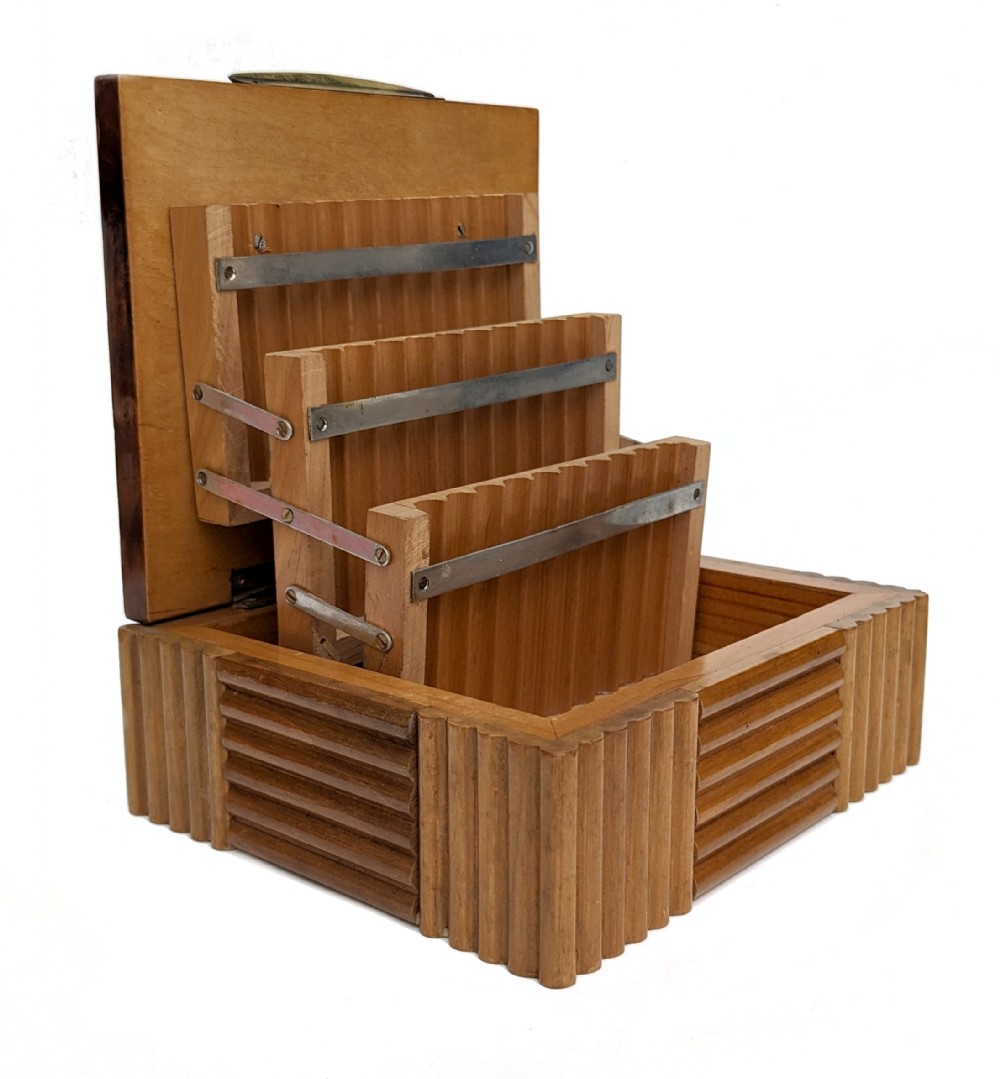 An open Art Deco walnut cigarette box featuring fluted exterior moulding and a tiered mechanical interior structure.