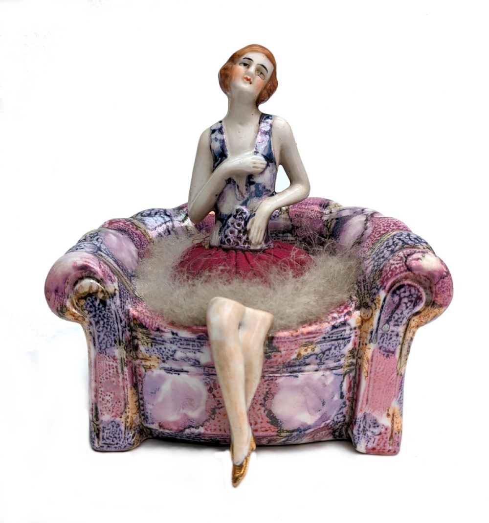 An Art Deco glazed ceramic powder puff stand modelled as a flapper lady seated in a pink and purple mottled armchair.