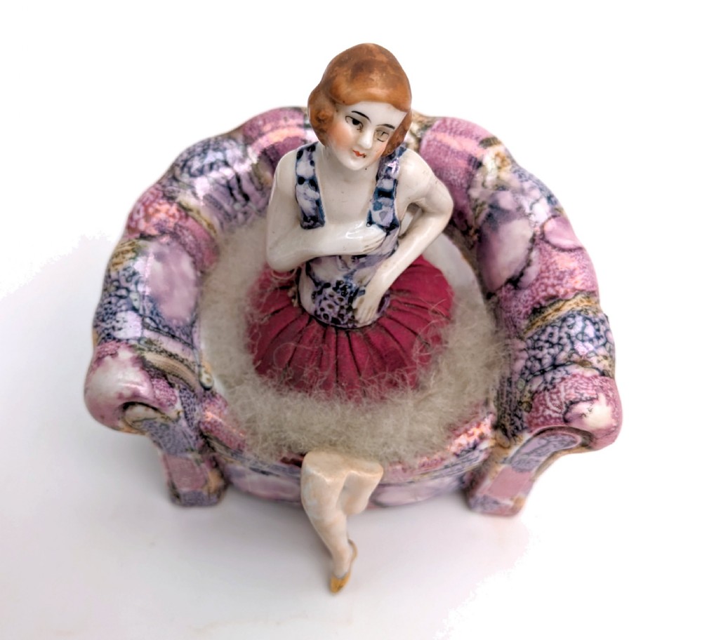 An Art Deco glazed ceramic powder puff stand modelled as a flapper lady seated in a pink and purple mottled armchair. View II
