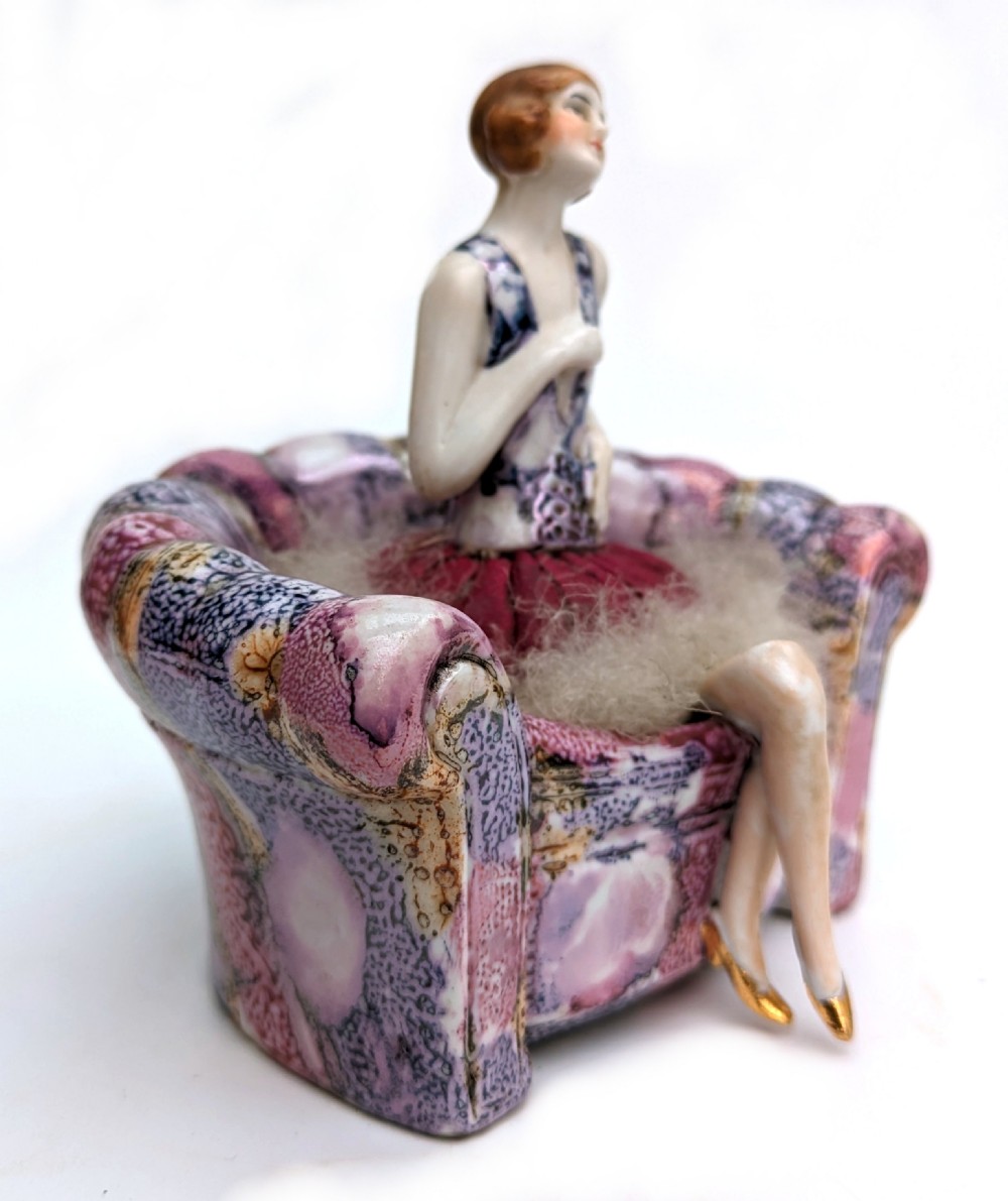 An Art Deco glazed ceramic powder puff stand modelled as a flapper lady seated in a pink and purple mottled armchair. View III