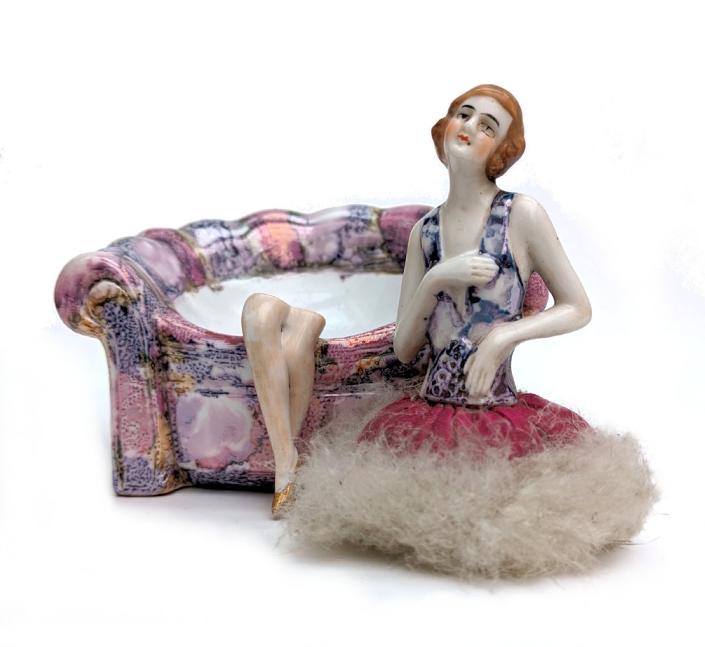 An Art Deco glazed ceramic powder puff stand modelled as a flapper lady seated in a pink and purple mottled armchair. View V