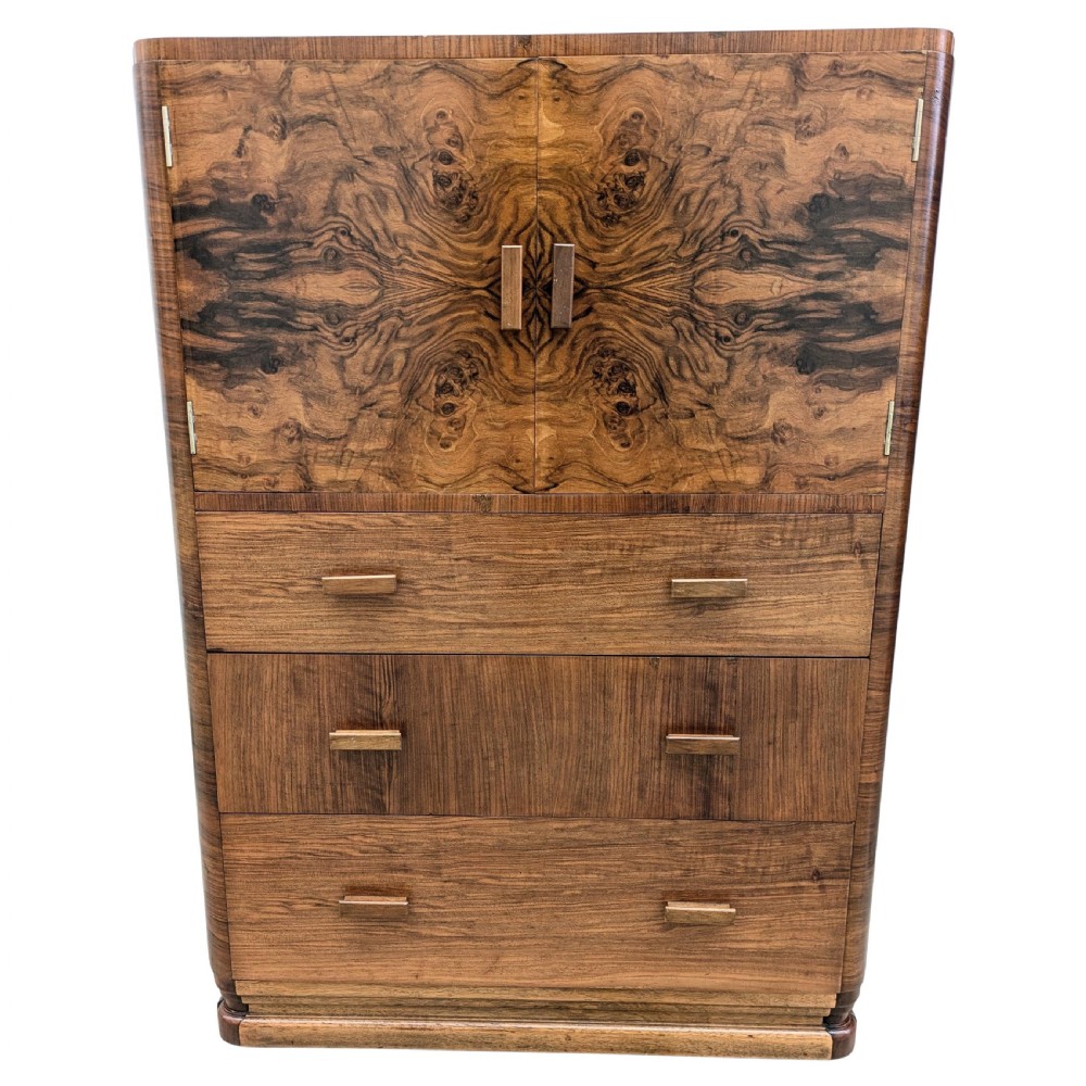 An English Art Deco tallboy crafted from figured burr walnut, featuring a top two-door cupboard above three full-width drawers with matching handles.
