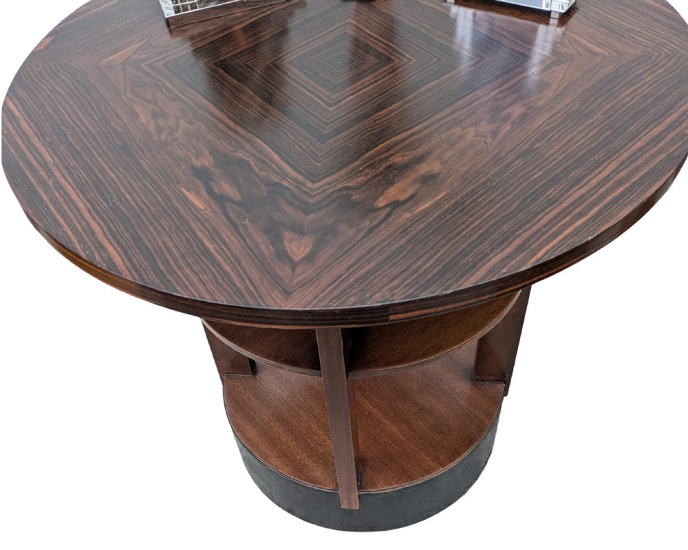 An Art Deco circular dark wood centre table featuring three tiered shelves supported by four vertical legs resting on a solid round base. View II