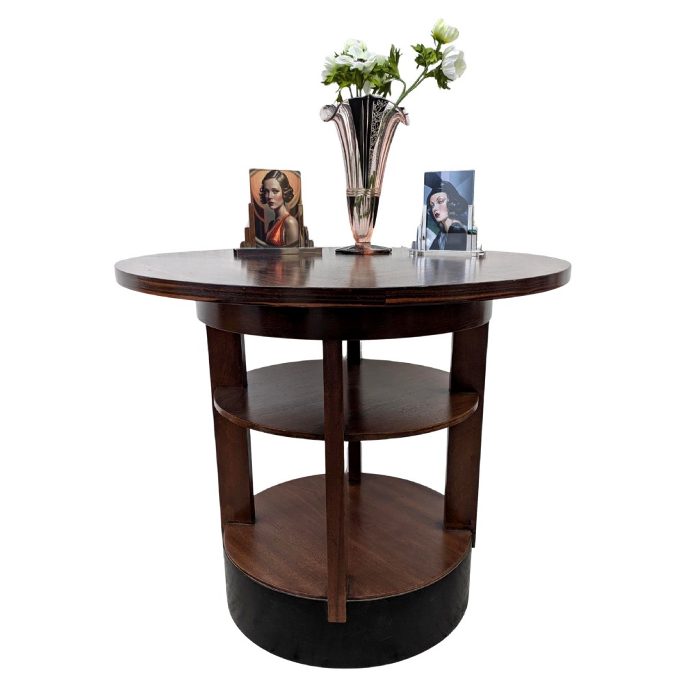 An Art Deco circular dark wood centre table featuring three tiered shelves supported by four vertical legs resting on a solid round base. View V