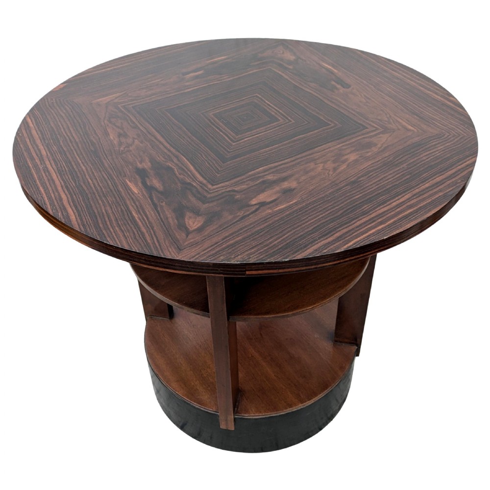An Art Deco circular dark wood centre table featuring three tiered shelves supported by four vertical legs resting on a solid round base. View VIII