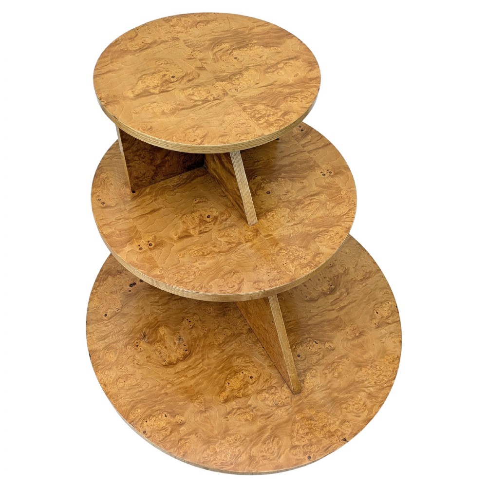 A matching pair of British Art Deco three-tiered modernist occasional tables featuring figured light brown wood veneer and architectural angular supports. View II