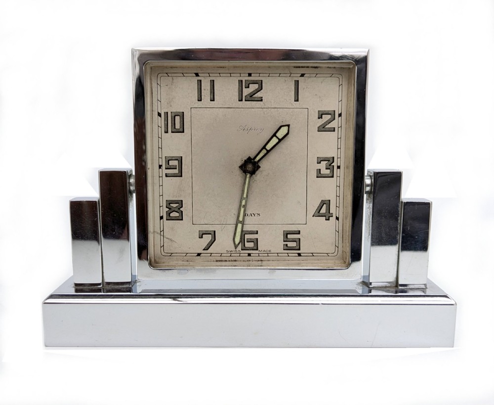 An Art Deco chrome desk clock featuring a rectangular face with geometric stepped side columns and stylized numerals.