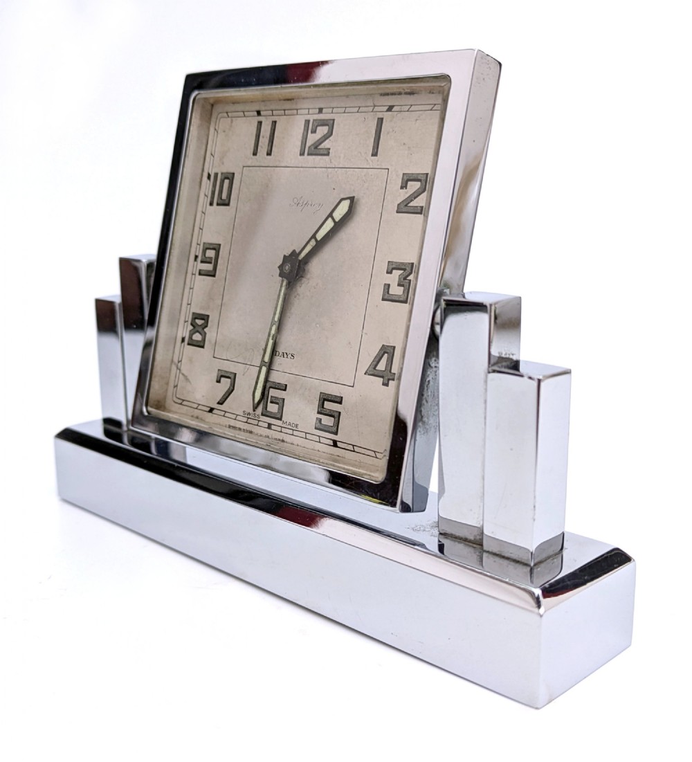 An Art Deco chrome desk clock featuring a rectangular face with geometric stepped side columns and stylized numerals. View II