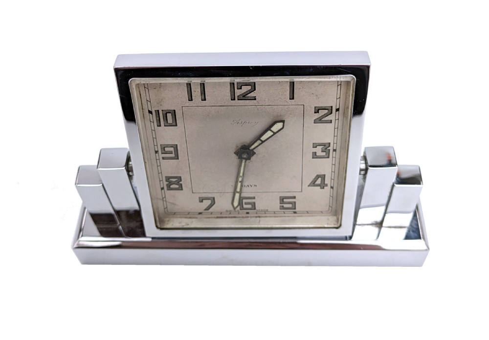 An Art Deco chrome desk clock featuring a rectangular face with geometric stepped side columns and stylized numerals. View III