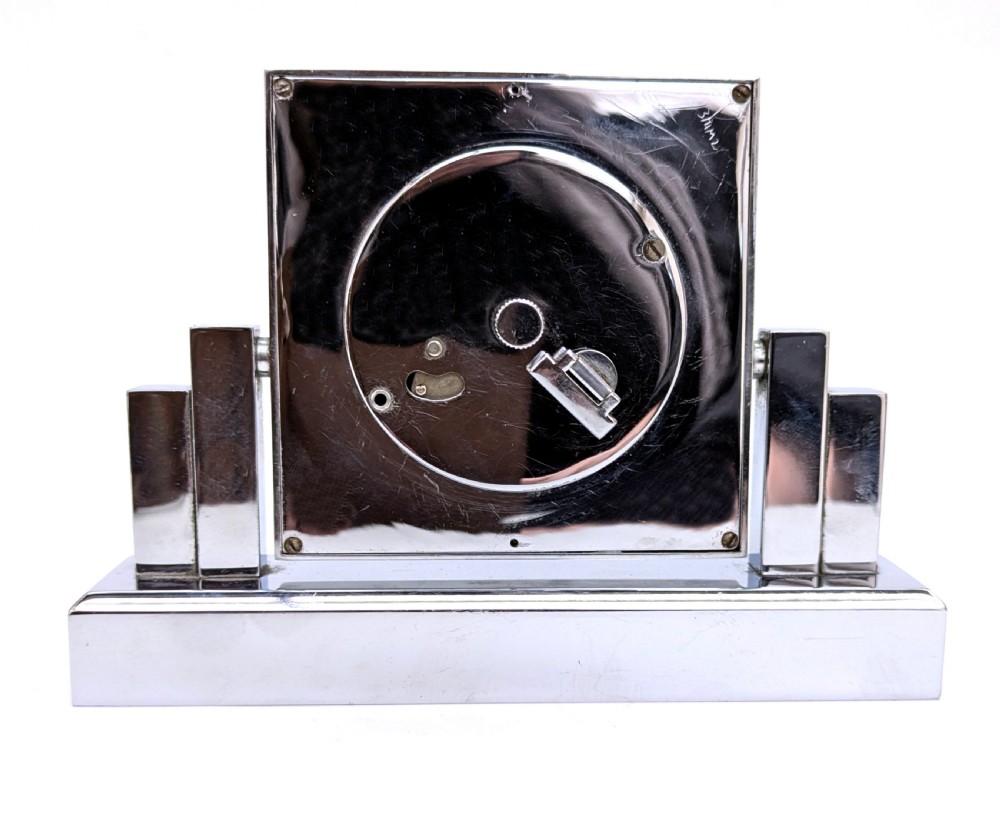 An Art Deco chrome desk clock featuring a rectangular face with geometric stepped side columns and stylized numerals. View IX