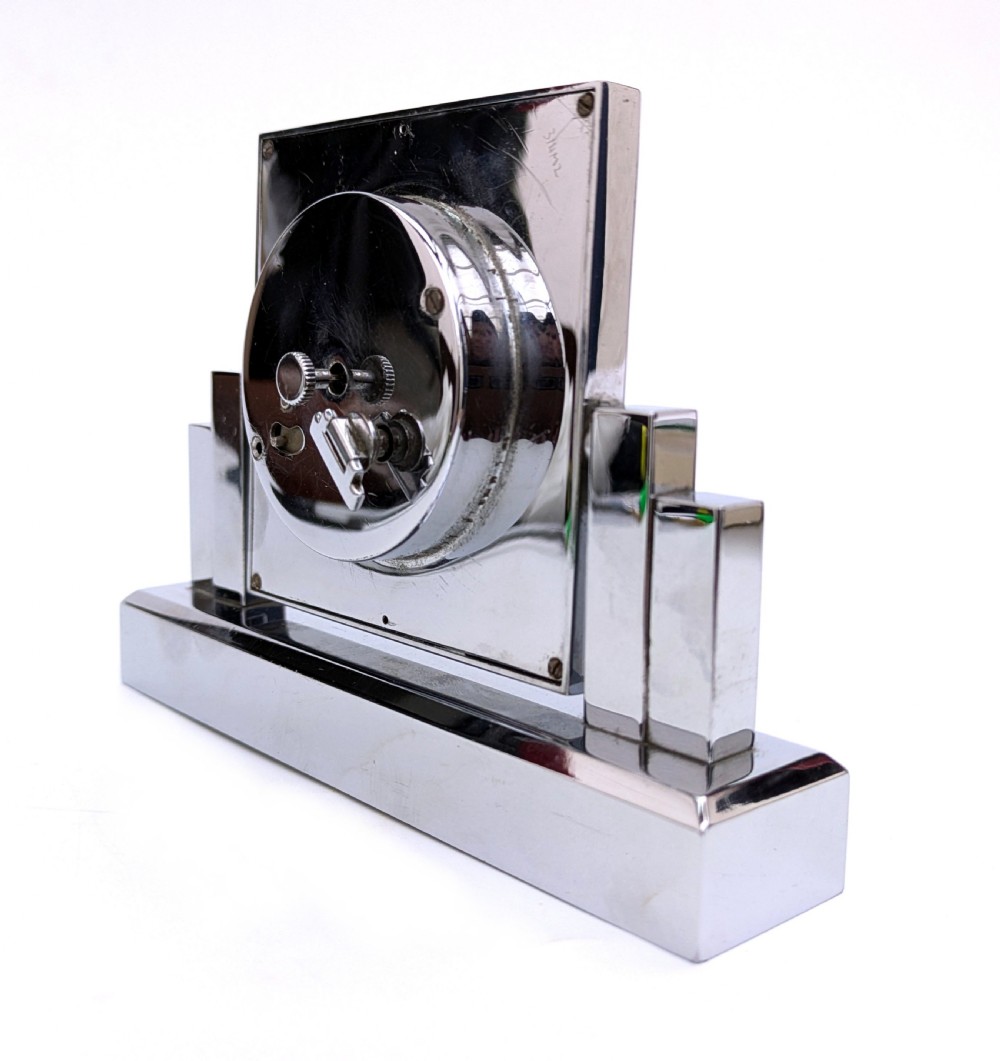 An Art Deco chrome desk clock featuring a rectangular face with geometric stepped side columns and stylized numerals. View X
