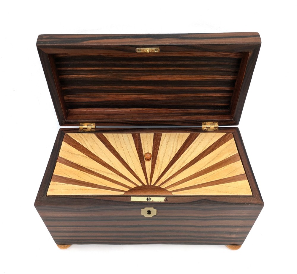 An open Art Deco dark wood tea caddy featuring a light wood sunburst inlay pattern on its internal lid. View II