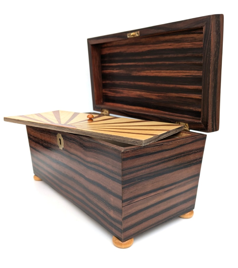 An open Art Deco dark wood tea caddy featuring a light wood sunburst inlay pattern on its internal lid. View IV