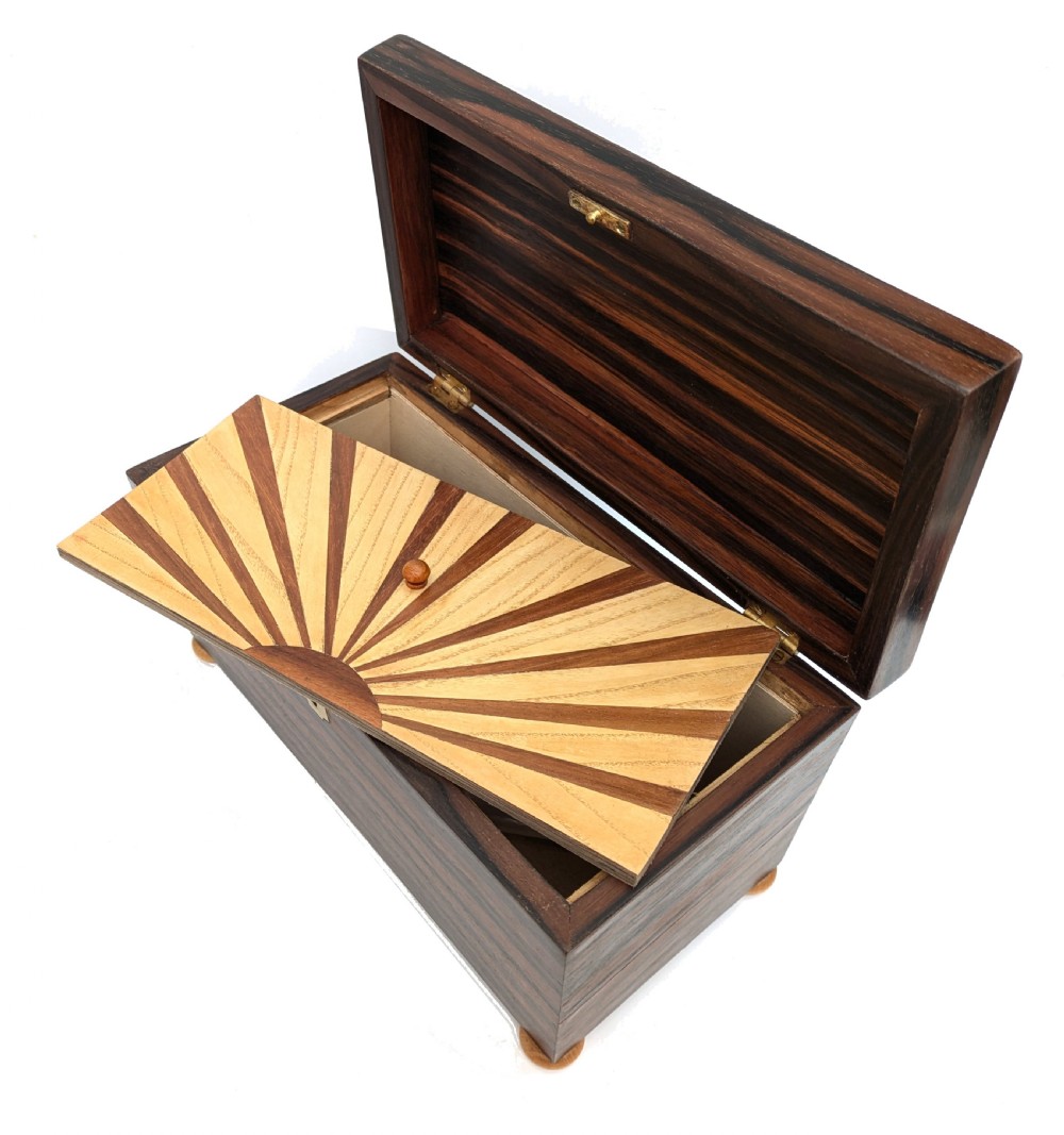 An open Art Deco dark wood tea caddy featuring a light wood sunburst inlay pattern on its internal lid. View V