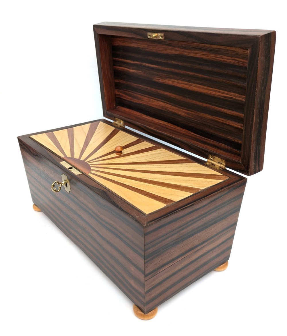 An open Art Deco dark wood tea caddy featuring a light wood sunburst inlay pattern on its internal lid. View VI