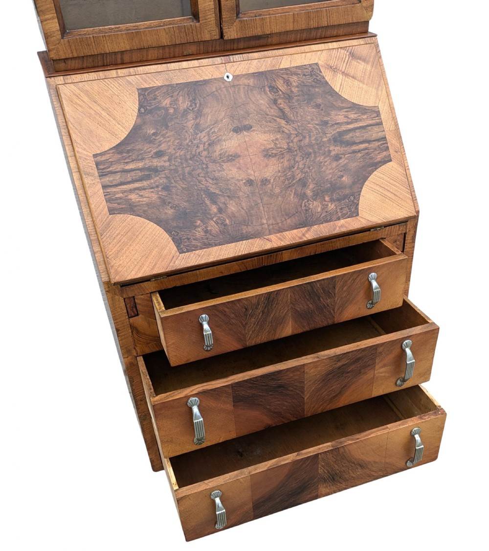 An Art Deco walnut upright bureau bookcase featuring a two-door glazed upper display cabinet above a slope-front writing slope and three drawers. View X