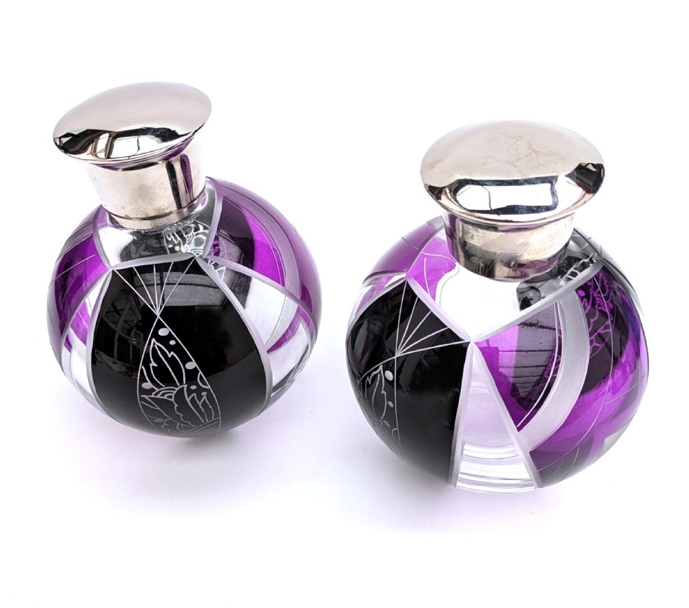 A pair of spherical glass Art Deco perfume bottles featuring purple and black geometric enamel panels with etched floral patterns and polished metal caps.