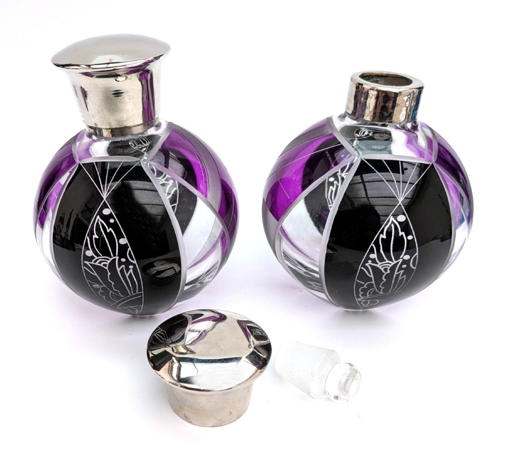 A pair of spherical glass Art Deco perfume bottles featuring purple and black geometric enamel panels with etched floral patterns and polished metal caps. View V