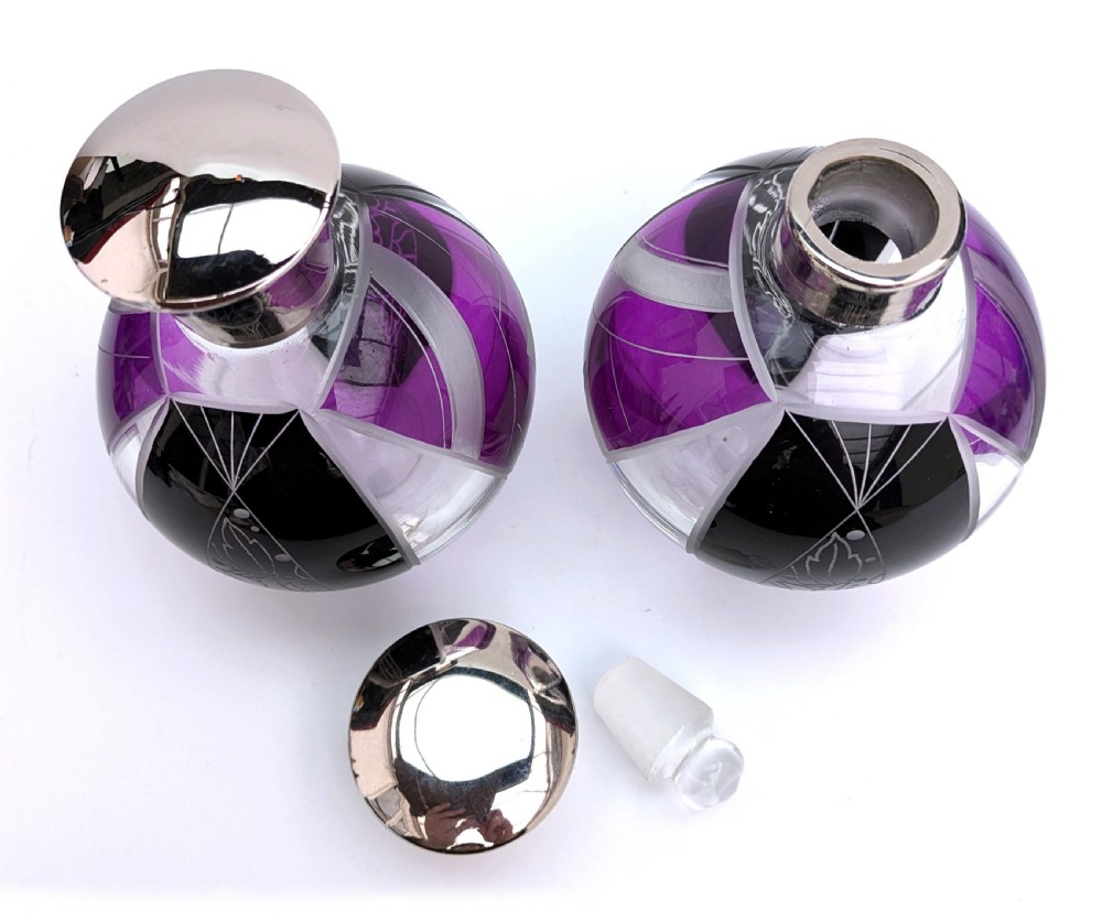 A pair of spherical glass Art Deco perfume bottles featuring purple and black geometric enamel panels with etched floral patterns and polished metal caps. View VI