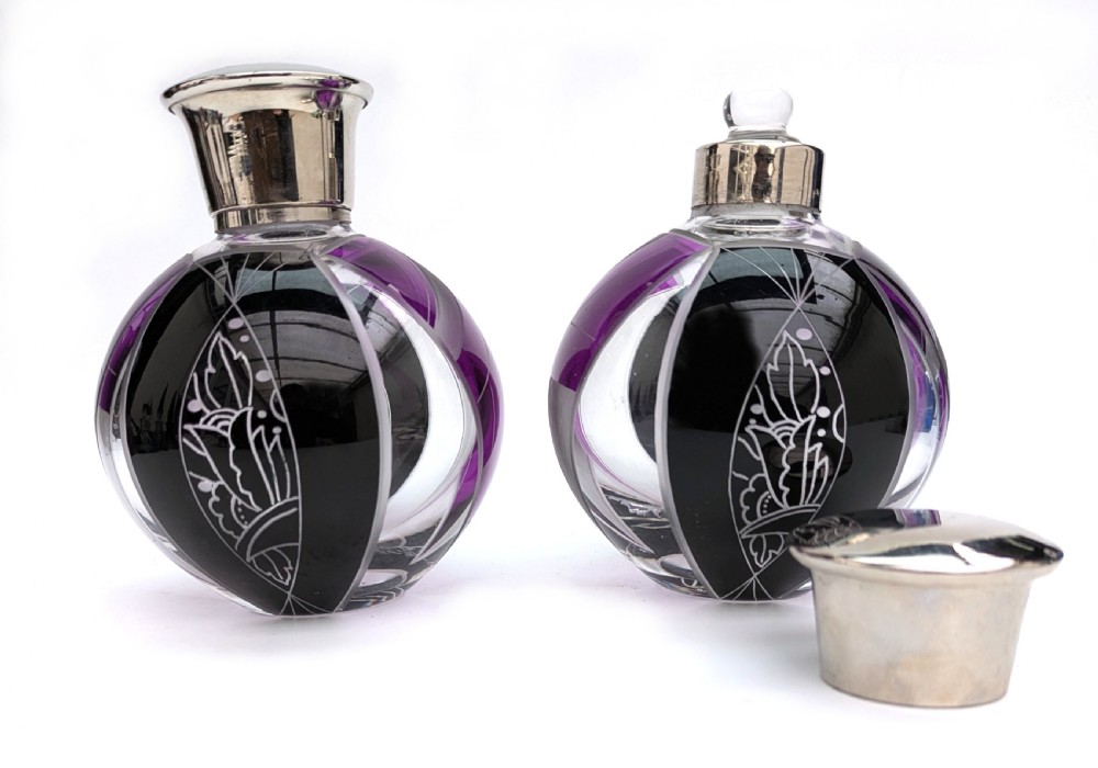 A pair of spherical glass Art Deco perfume bottles featuring purple and black geometric enamel panels with etched floral patterns and polished metal caps. View VII