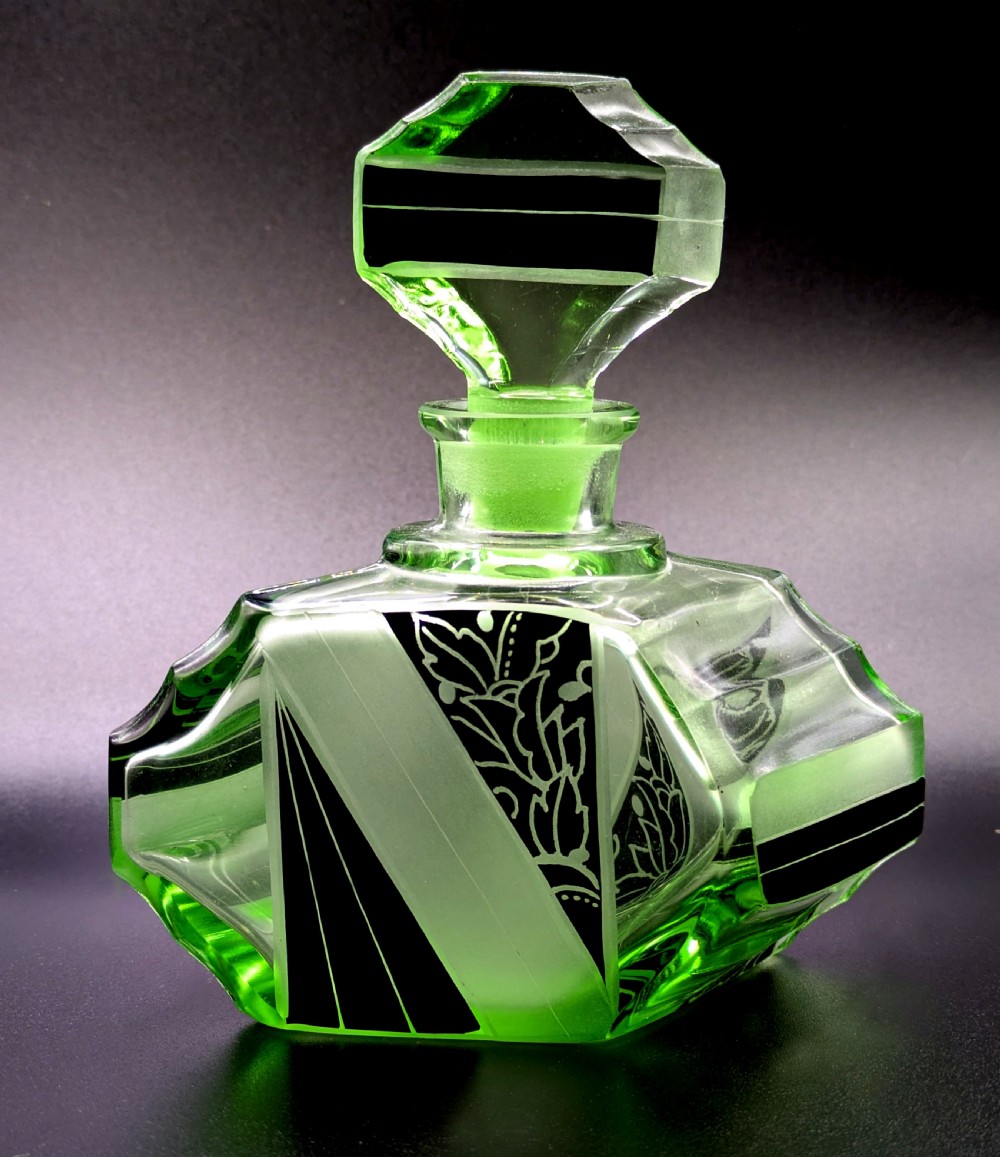 An Art Deco green glass perfume bottle featuring geometric black enamel and frosted foliage patterns with a faceted glass stopper.