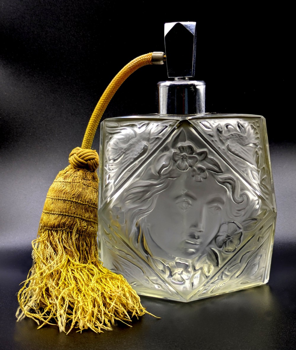 A faceted clear glass Art Deco scent bottle featuring a relief-moulded womans face and a gold fabric atomiser bulb with tassel. View II