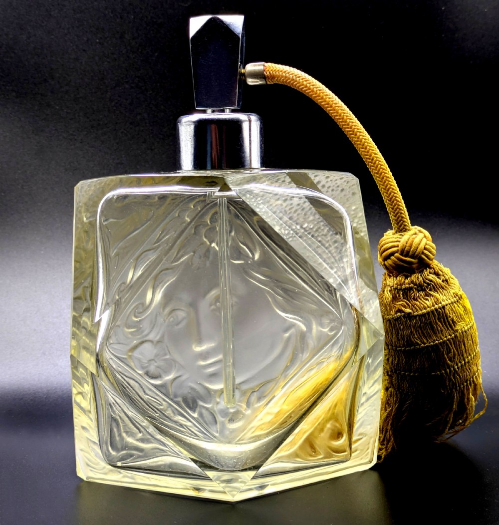 A faceted clear glass Art Deco scent bottle featuring a relief-moulded womans face and a gold fabric atomiser bulb with tassel. View VI