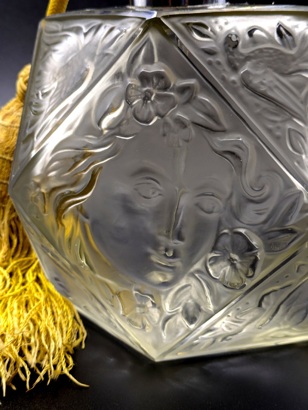 A faceted clear glass Art Deco scent bottle featuring a relief-moulded womans face and a gold fabric atomiser bulb with tassel. View VII