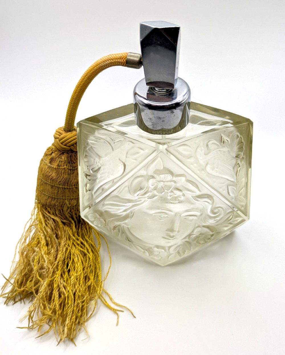 A faceted clear glass Art Deco scent bottle featuring a relief-moulded womans face and a gold fabric atomiser bulb with tassel. View XI