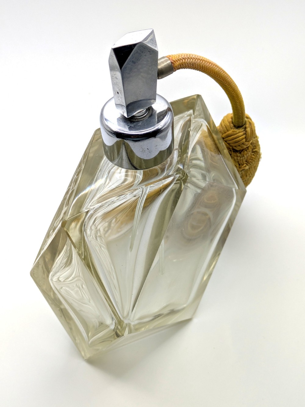 A faceted clear glass Art Deco scent bottle featuring a relief-moulded womans face and a gold fabric atomiser bulb with tassel. View XIV