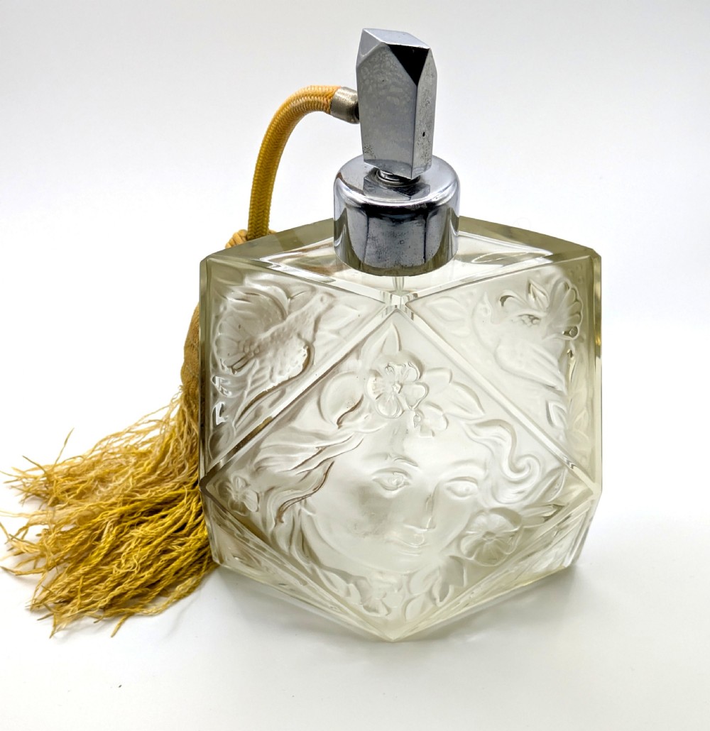 A faceted clear glass Art Deco scent bottle featuring a relief-moulded womans face and a gold fabric atomiser bulb with tassel. View XV