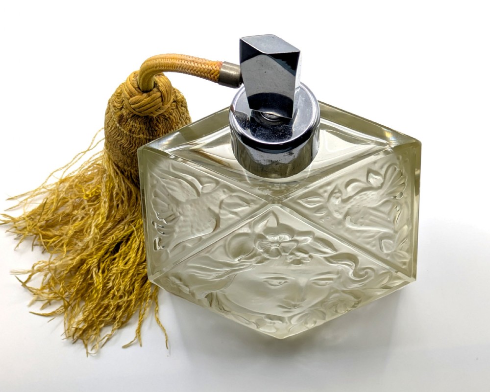 A faceted clear glass Art Deco scent bottle featuring a relief-moulded womans face and a gold fabric atomiser bulb with tassel. View XVII