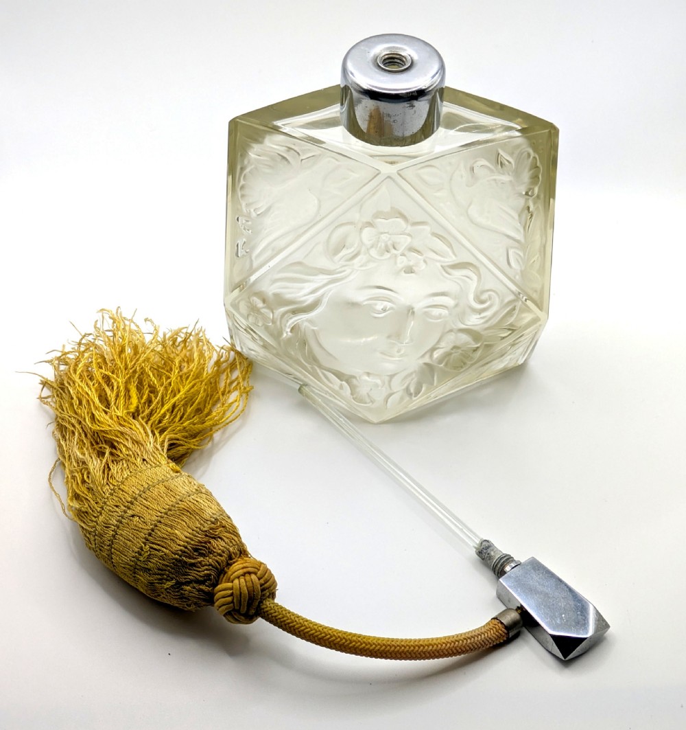 A faceted clear glass Art Deco scent bottle featuring a relief-moulded womans face and a gold fabric atomiser bulb with tassel. View XVIII