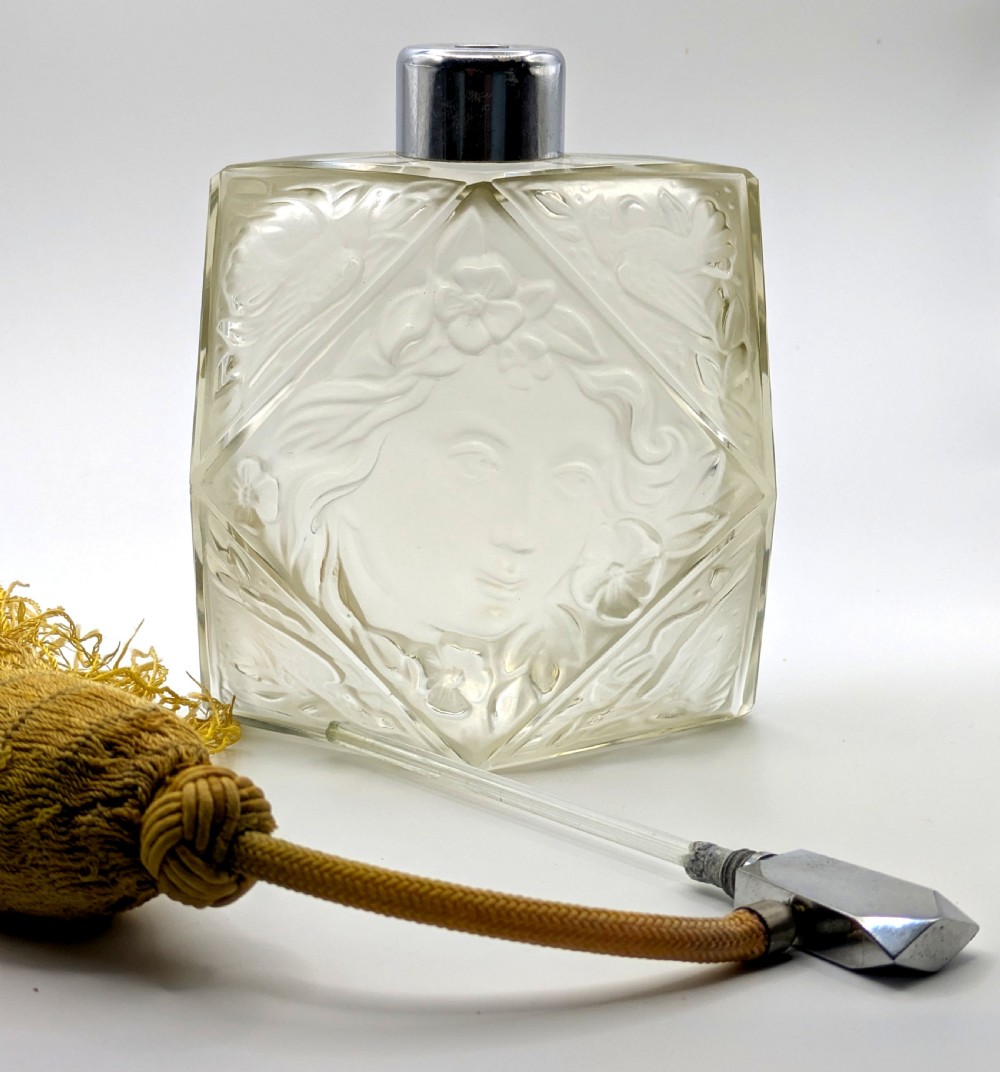 A faceted clear glass Art Deco scent bottle featuring a relief-moulded womans face and a gold fabric atomiser bulb with tassel. View XIX