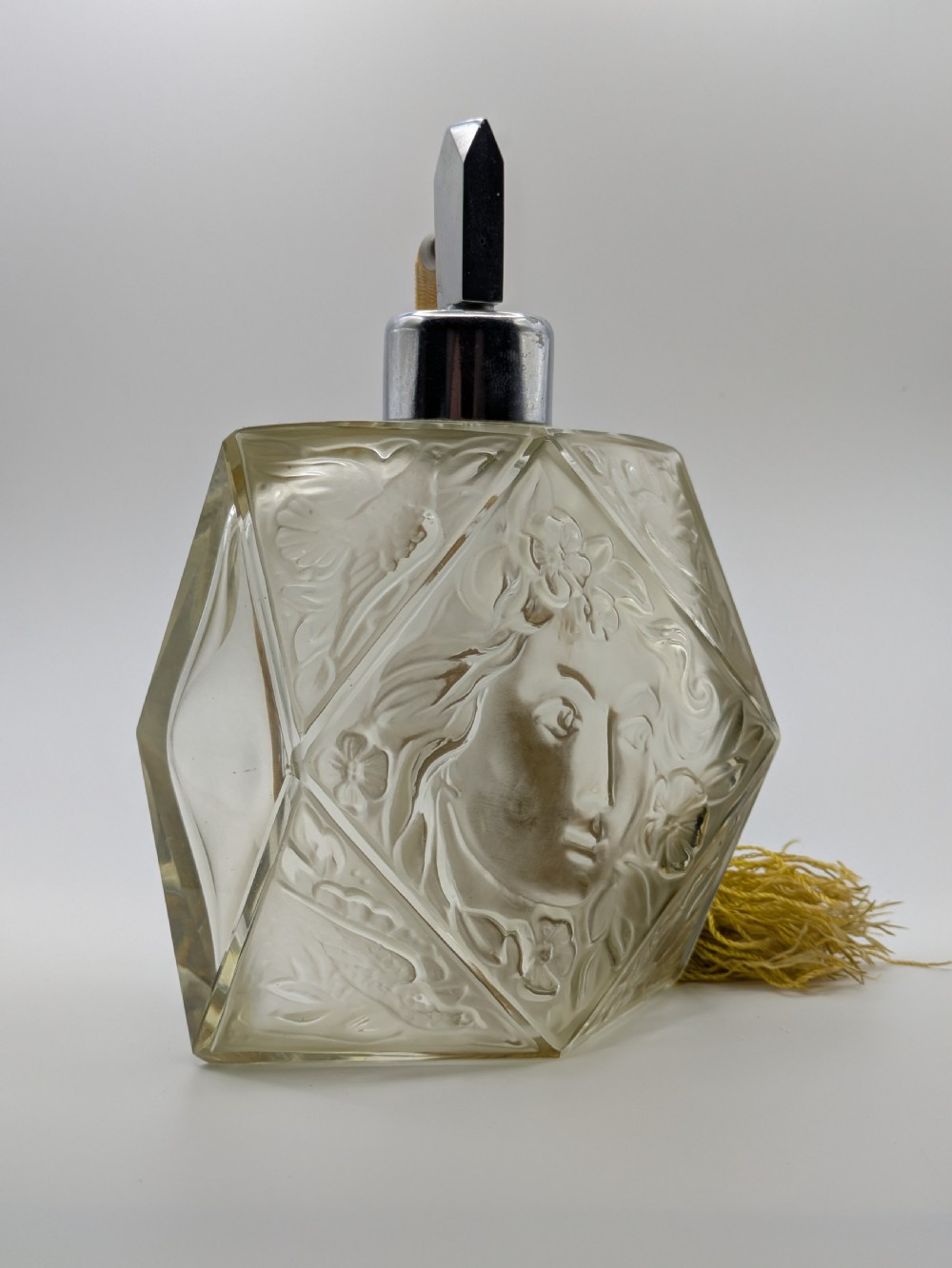 A faceted clear glass Art Deco scent bottle featuring a relief-moulded womans face and a gold fabric atomiser bulb with tassel. View XXIII