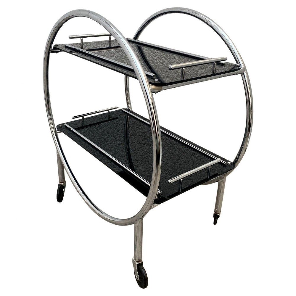 An Art Deco circular chrome hostess trolley featuring two textured black glass tiers set within twin hoop frames on castors.