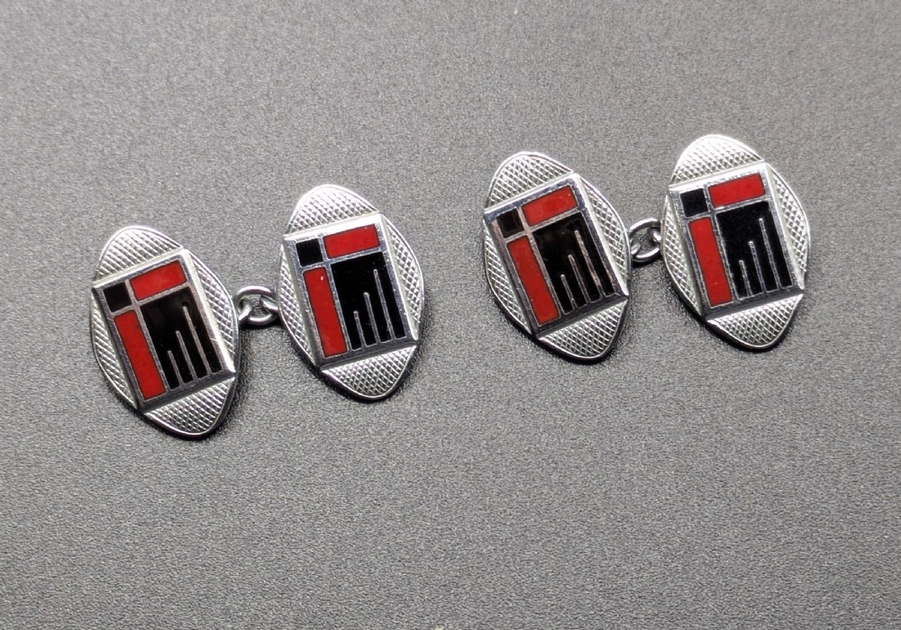 A pair of oval Art Deco cufflinks made of silver-coloured metal featuring geometric red and black enamel patterns surrounded by an engine-turned border. View II
