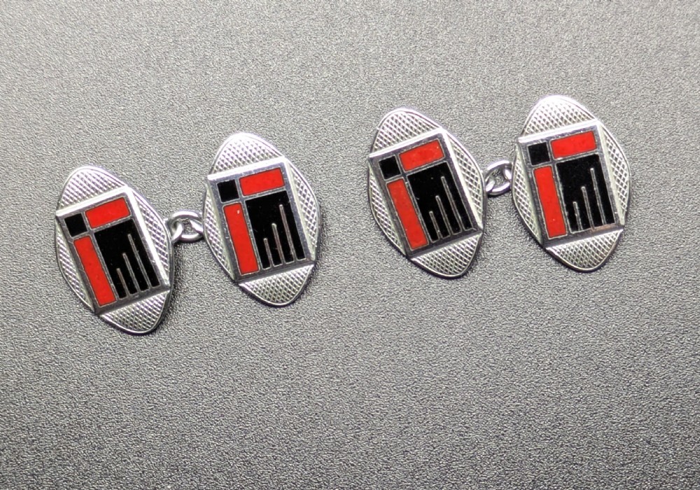 A pair of oval Art Deco cufflinks made of silver-coloured metal featuring geometric red and black enamel patterns surrounded by an engine-turned border. View III