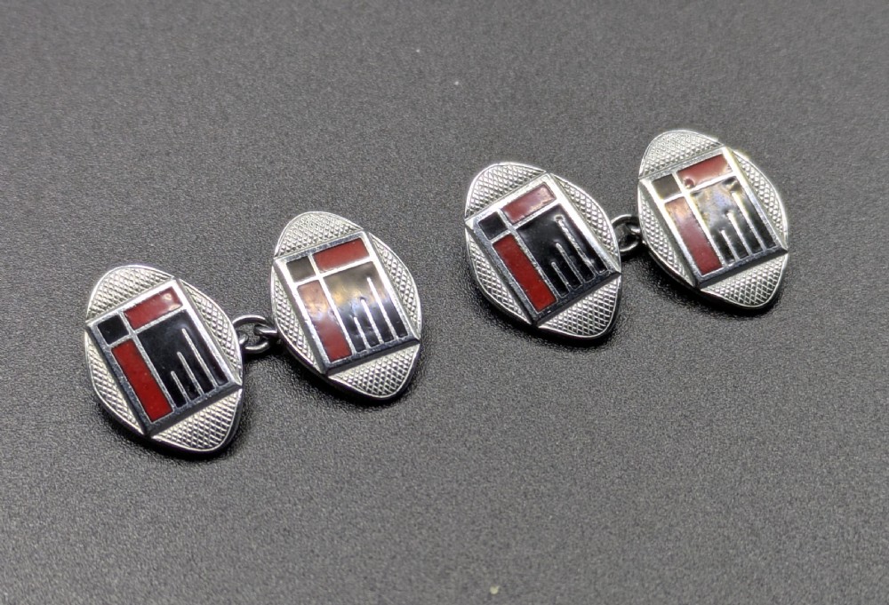 A pair of oval Art Deco cufflinks made of silver-coloured metal featuring geometric red and black enamel patterns surrounded by an engine-turned border. View IV