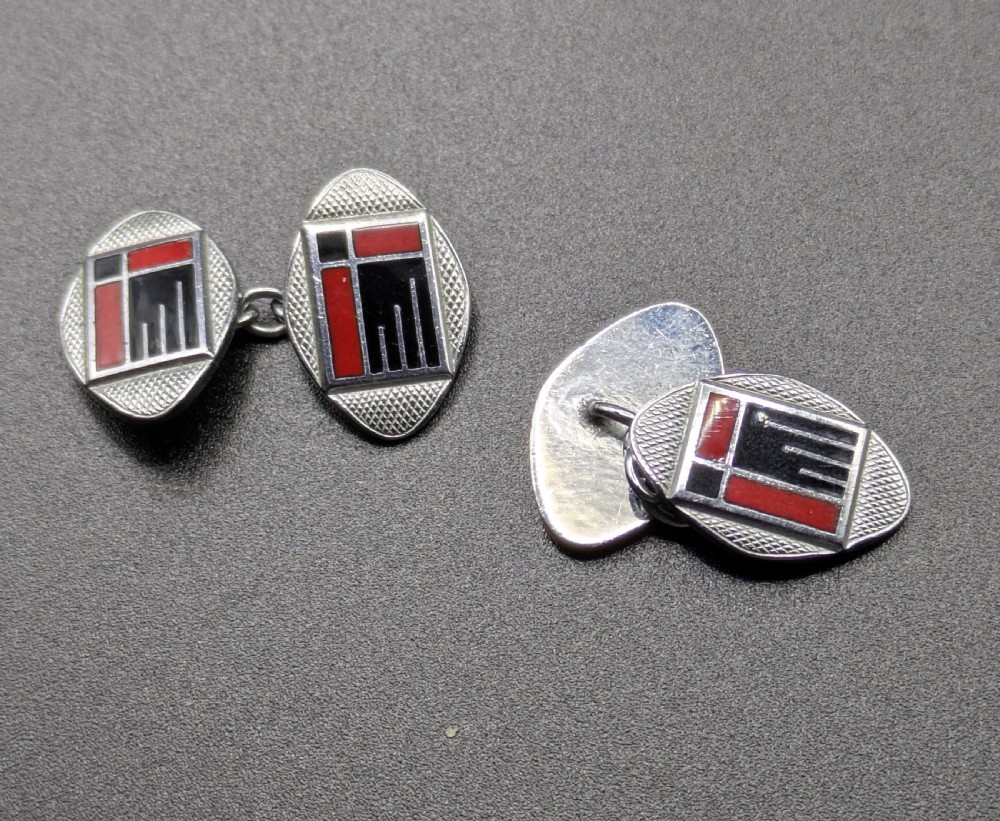 A pair of oval Art Deco cufflinks made of silver-coloured metal featuring geometric red and black enamel patterns surrounded by an engine-turned border. View V