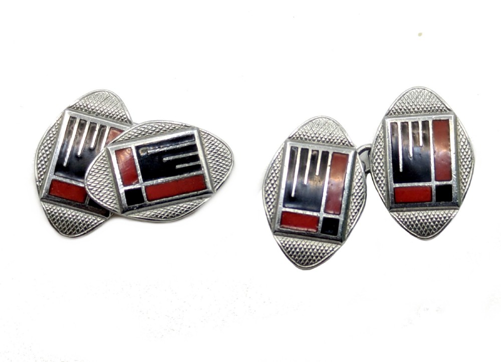 A pair of oval Art Deco cufflinks made of silver-coloured metal featuring geometric red and black enamel patterns surrounded by an engine-turned border. View VI