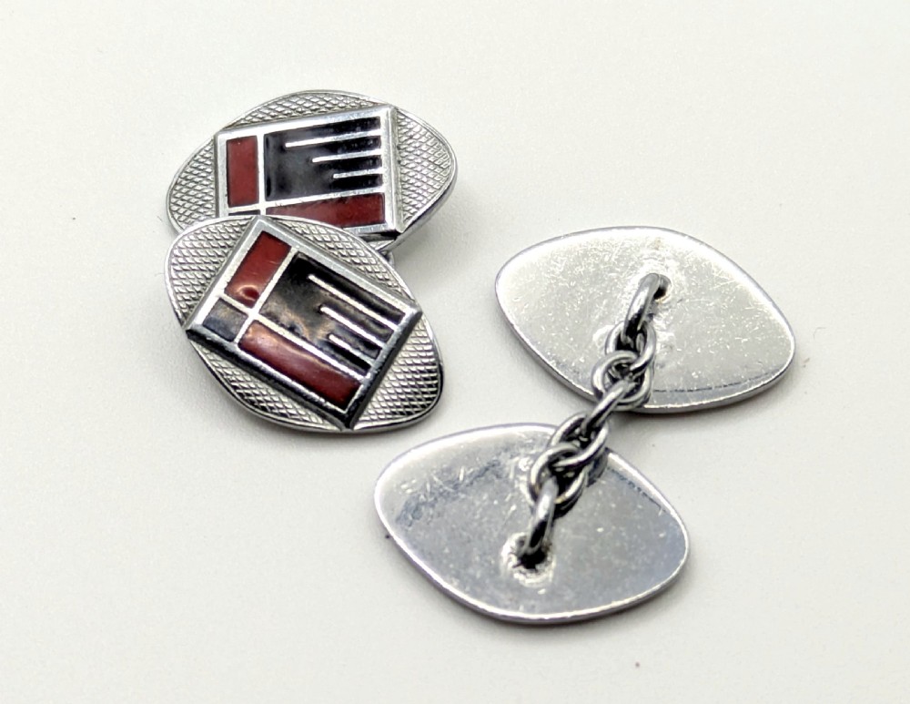 A pair of oval Art Deco cufflinks made of silver-coloured metal featuring geometric red and black enamel patterns surrounded by an engine-turned border. View VIII