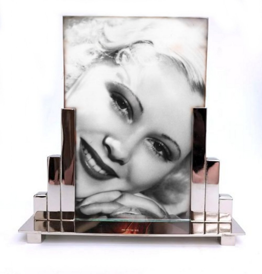 An Art Deco nickel-plated picture frame with stepped geometric side supports holding a black and white portrait photo on a silver metal base.